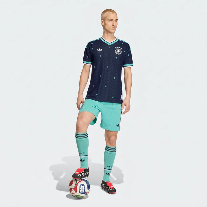 Male model wearing the Germany 26 Away Authentic Jersey in navy blue with light blue shorts and socks, posing with a soccer