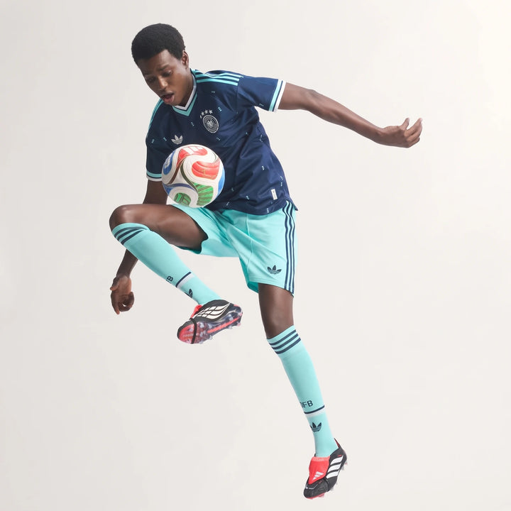 Male model in a navy blue Germany 26 Away Authentic Jersey with light blue shorts and socks, juggling a soccer ball in