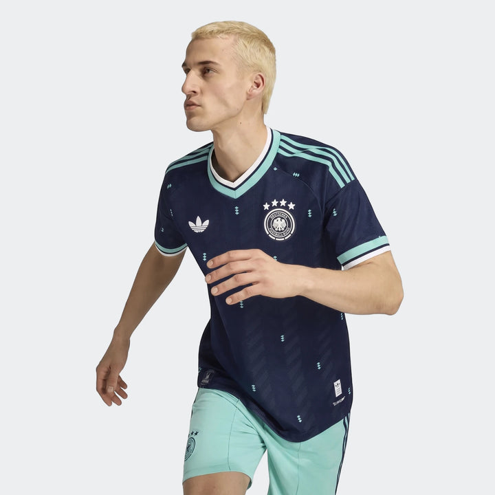 Young male model in navy blue Adidas Germany 26 Away Authentic Jersey with light green accents and shorts.