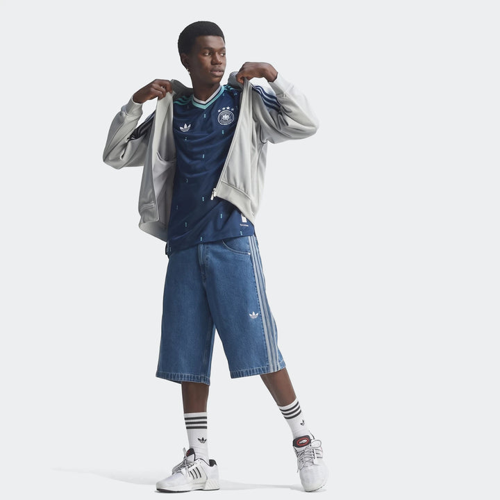 Male model wearing a navy blue Germany 26 Away Authentic Jersey, light gray hoodie, blue denim shorts, and white sneakers.