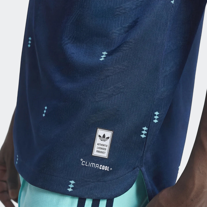 Close-up of a person wearing a navy blue Adidas Germany 26 Away Authentic Jersey with light blue patterned details.