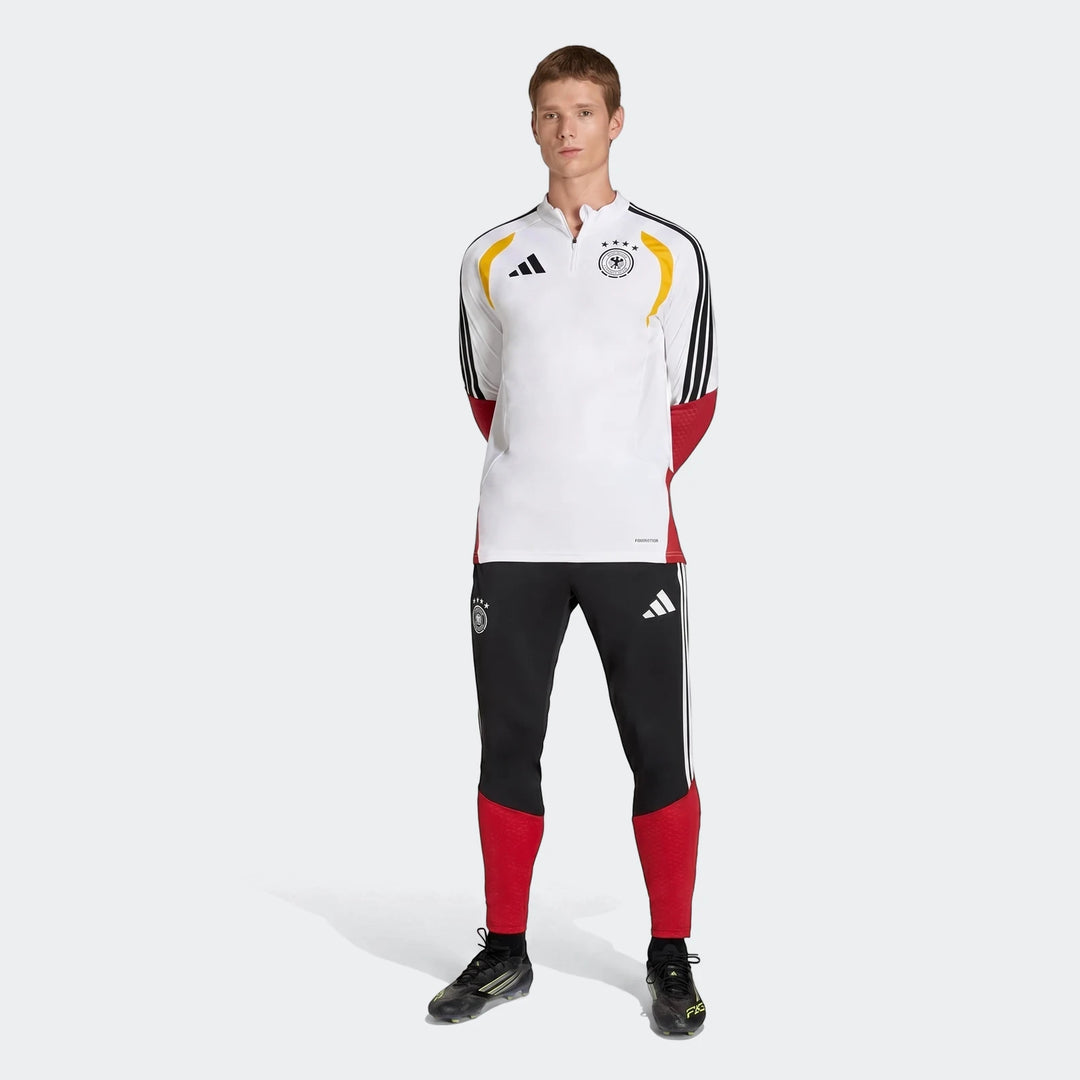 Male model wearing white, yellow, black, and red Germany 26 Tiro Training Top and black training pants, full body view.