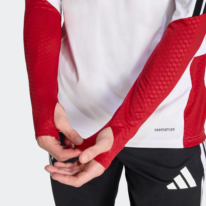 Germany 26 Tiro Training Top in white and red, featuring long sleeves with thumbholes, modeled by a person adjusting the