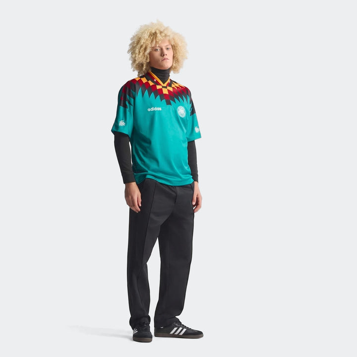 Model in the Germany Away Jersey 1994, a teal shirt with a vibrant black, red, and yellow geometric pattern.