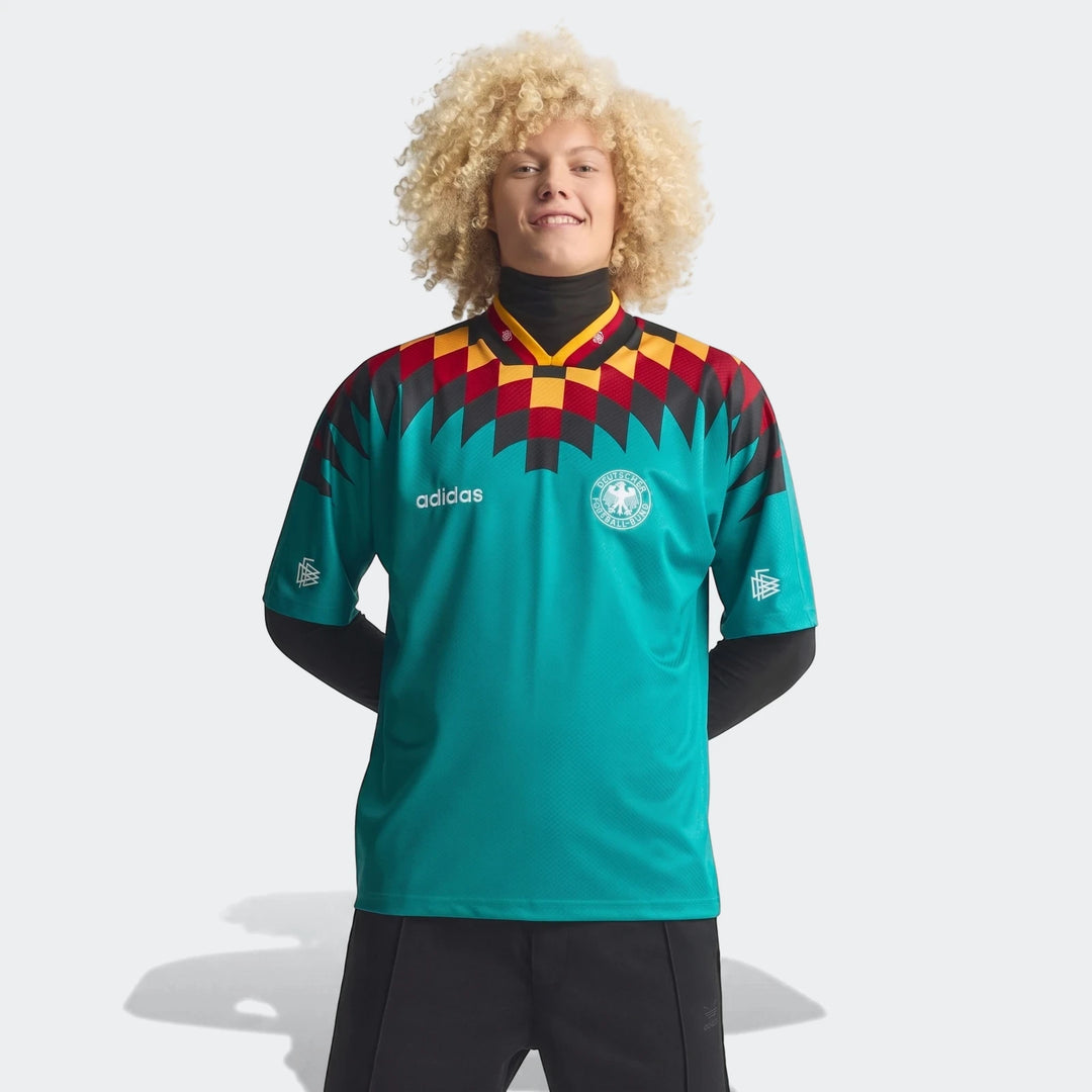 Germany Away Jersey 1994, teal with black, red, and yellow geometric pattern, worn by a smiling male model with curly hair.
