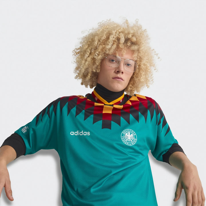 Front view of a model wearing the teal Germany Away Jersey from 1994 with black, red, and yellow geometric patterns.