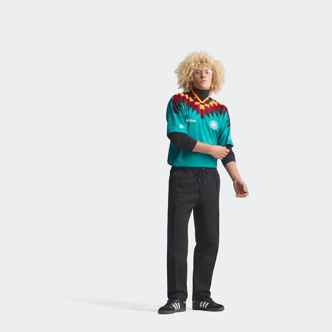 Male model wearing a full Germany Away Jersey 1994 in teal green with a red, yellow, and black geometric pattern.