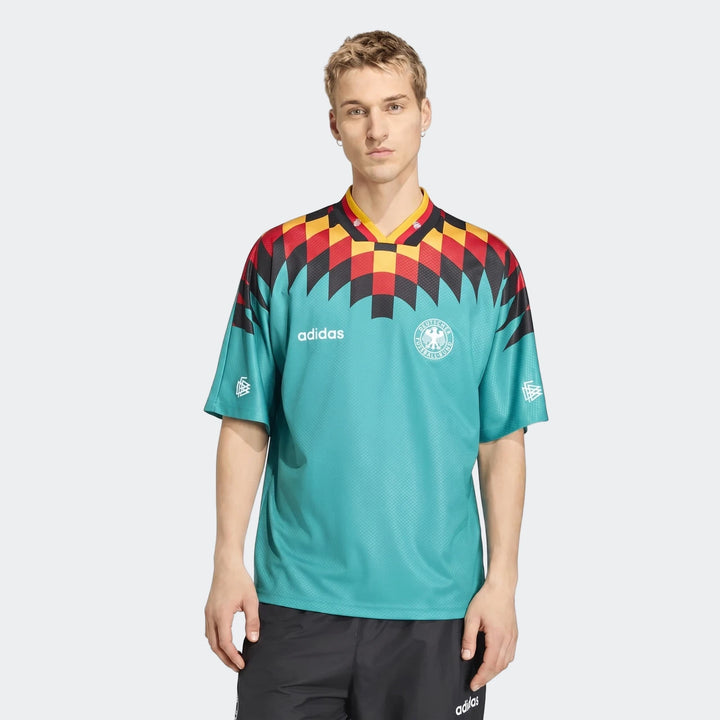 Male model wearing the turquoise Germany Away Jersey 1994 with a black, red, and yellow checkerboard pattern.