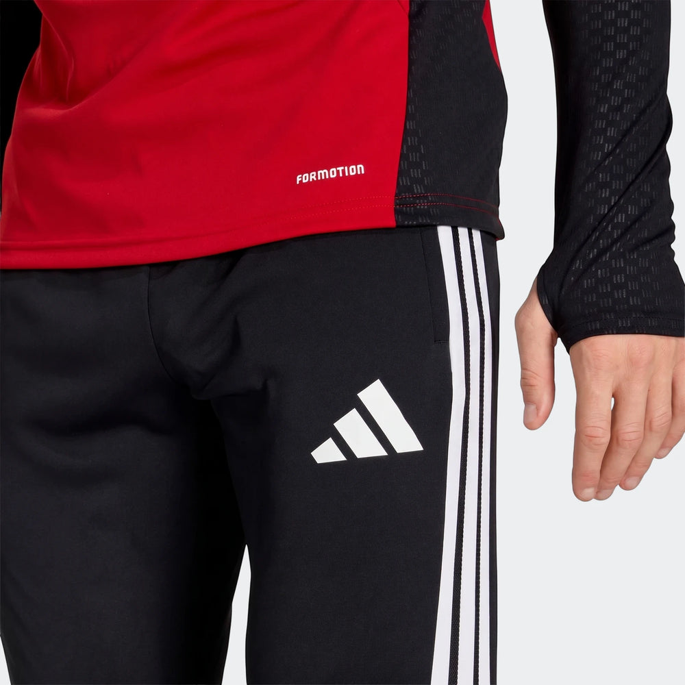 Close-up of black Adidas Germany Training Pants with white side stripes and logo, worn by a person with a red long-sleeve