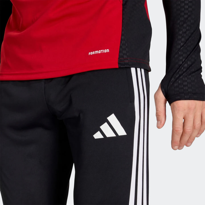 Close-up of black Adidas Germany Training Pants with white side stripes and logo, worn by a person with a red long-sleeve