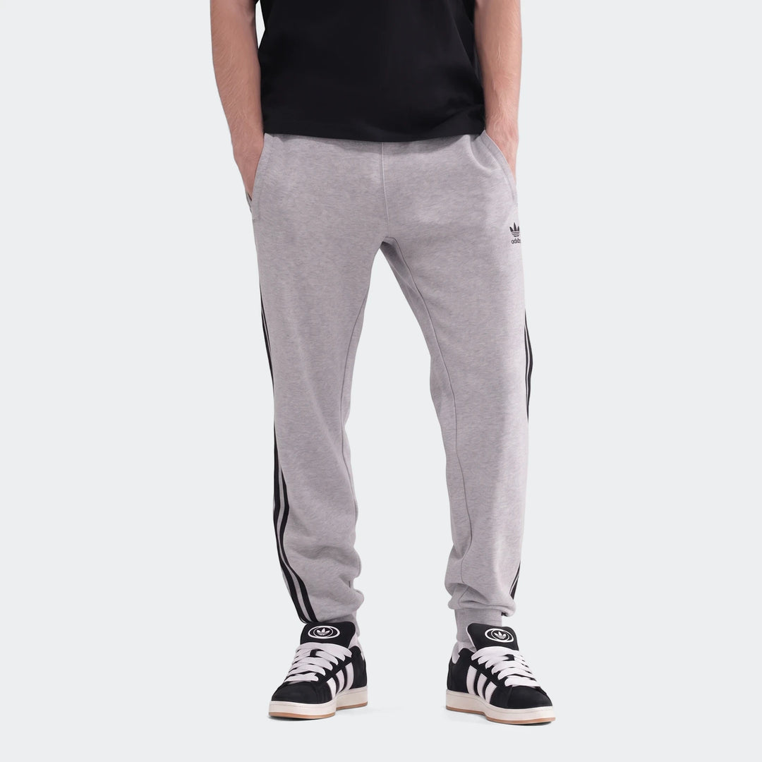 Gray Adidas 3-Stripes sweatpants worn by a male model, featuring black side stripes and a trefoil logo, paired with black