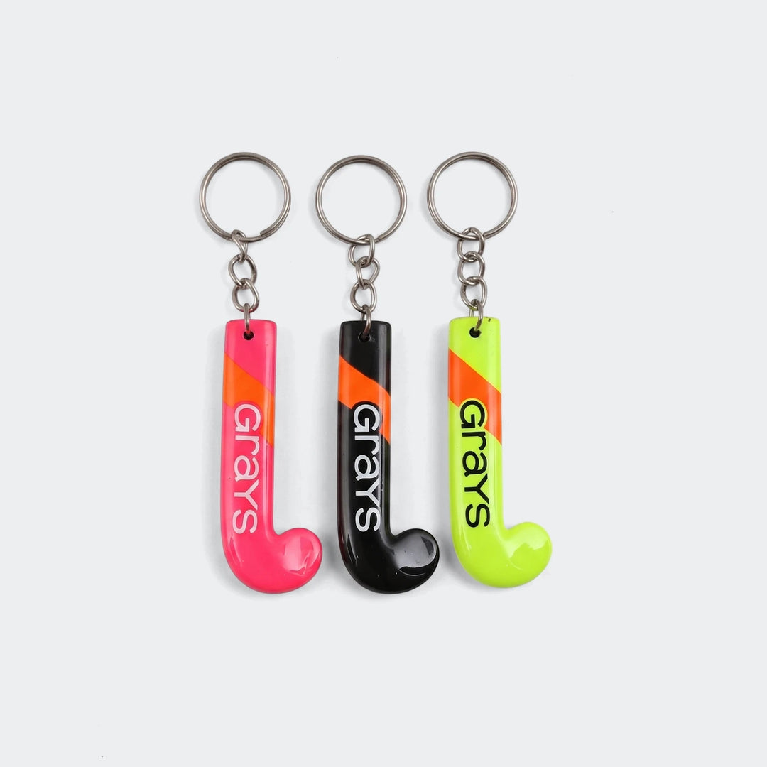 Three Grays field hockey stick keyrings in pink, black, and neon yellow, each with an orange stripe and metal ring.