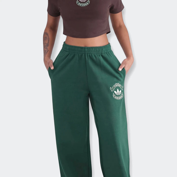 Person in green Adidas Infill Heritage Pants and a brown crop top, hands in pockets, waist-up view.