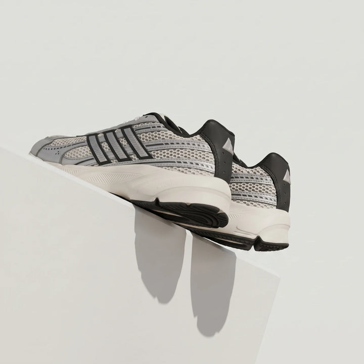 Close-up of light grey and black athletic sneakers with mesh details and a chunky sole, resting on a white surface.