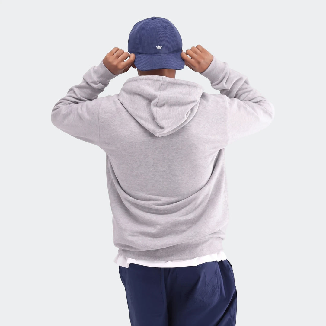 Rear view of a person wearing a grey Trefoil Hoodie and a blue corduroy cap, adjusting the cap with both hands.
