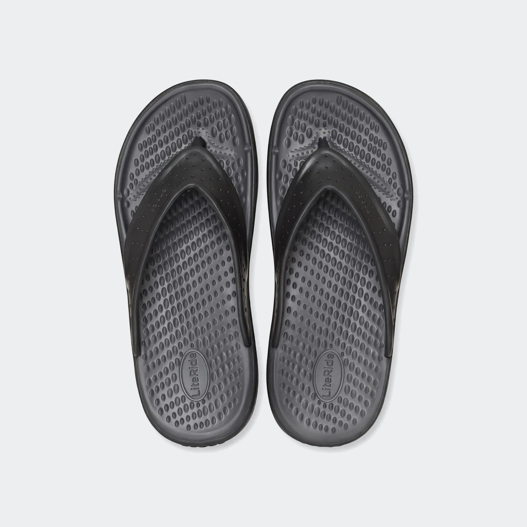 Pair of black In Motion Lite Ride flip-flops with textured footbeds and perforated straps, laid flat on a white background.
