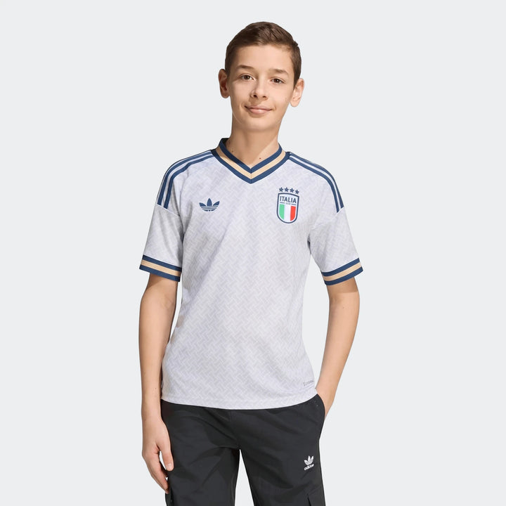 Youth Italy 25/26 Away Jersey worn by a boy, featuring a white patterned fabric, blue and gold V-neck collar, and team crest.