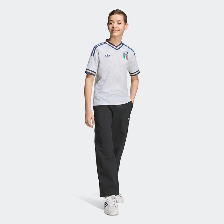 A young boy models the white Adidas Italy 25/26 Away Youth Jersey, paired with black cargo pants and white sneakers, shown