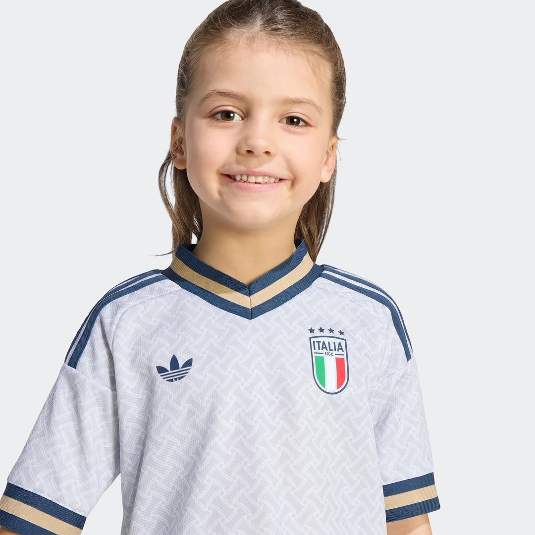 Smiling young girl wearing the official Italy 25/26 Away Mini Kit jersey. White with blue and gold trim, Adidas logo and