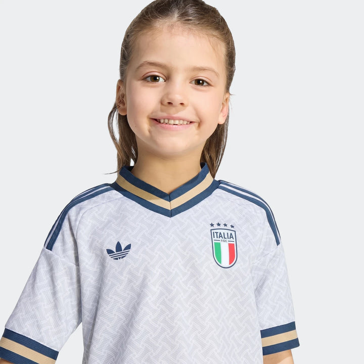 Smiling young girl wearing the official Italy 25/26 Away Mini Kit jersey. White with blue and gold trim, Adidas logo and