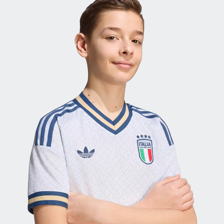 Young boy wearing a white Italy 25/26 Away Youth Soccer Jersey with blue and gold accents, front view.