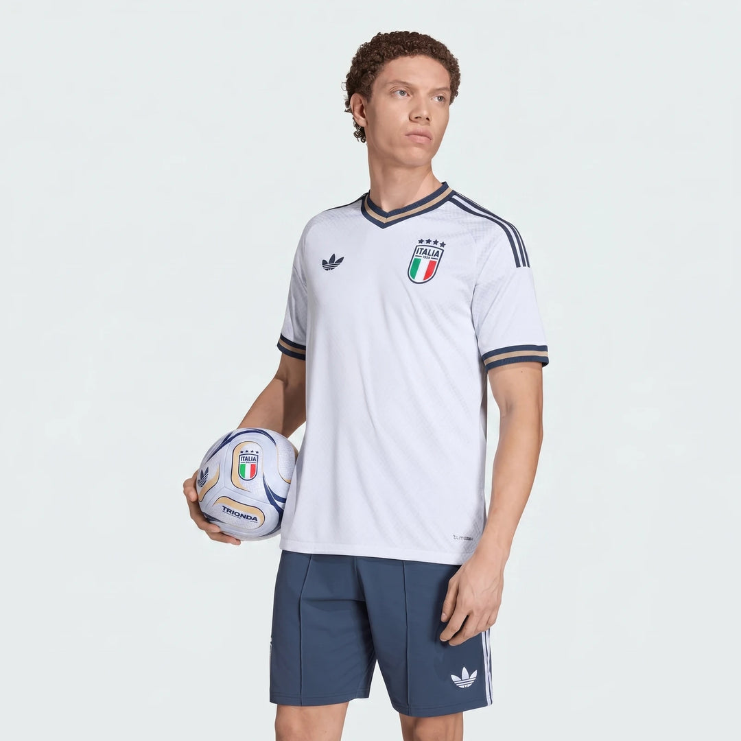Male model in white Italy national football team jersey and navy shorts holding a white and blue football.