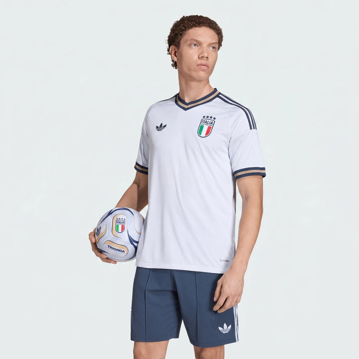 Male model in white Italy national football team jersey and navy shorts holding a white and blue football.
