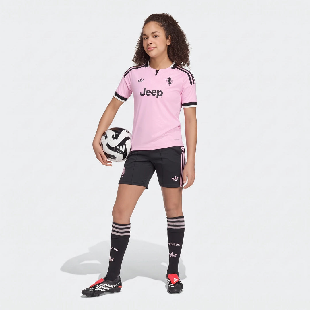 Young girl models a pink and black Juventus 26/27 Away Soccer Jersey for kids, complete with matching shorts, socks, and