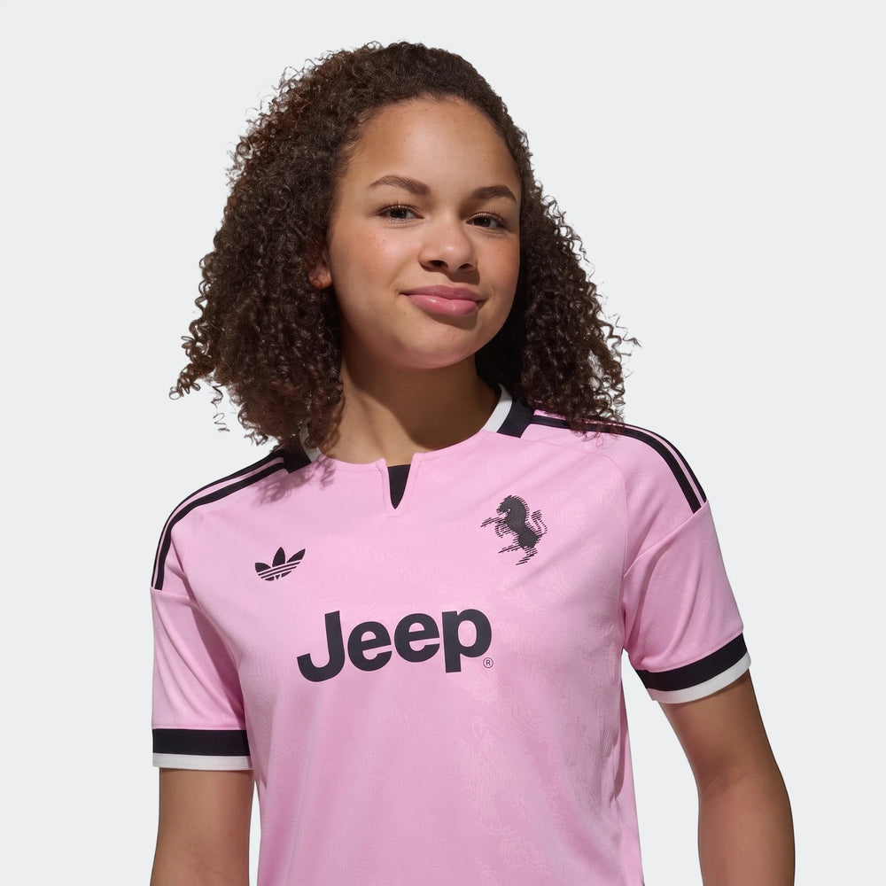 Pink short-sleeve Adidas Juventus 26/27 away jersey for kids, featuring sponsor and club logos, modeled by a child.