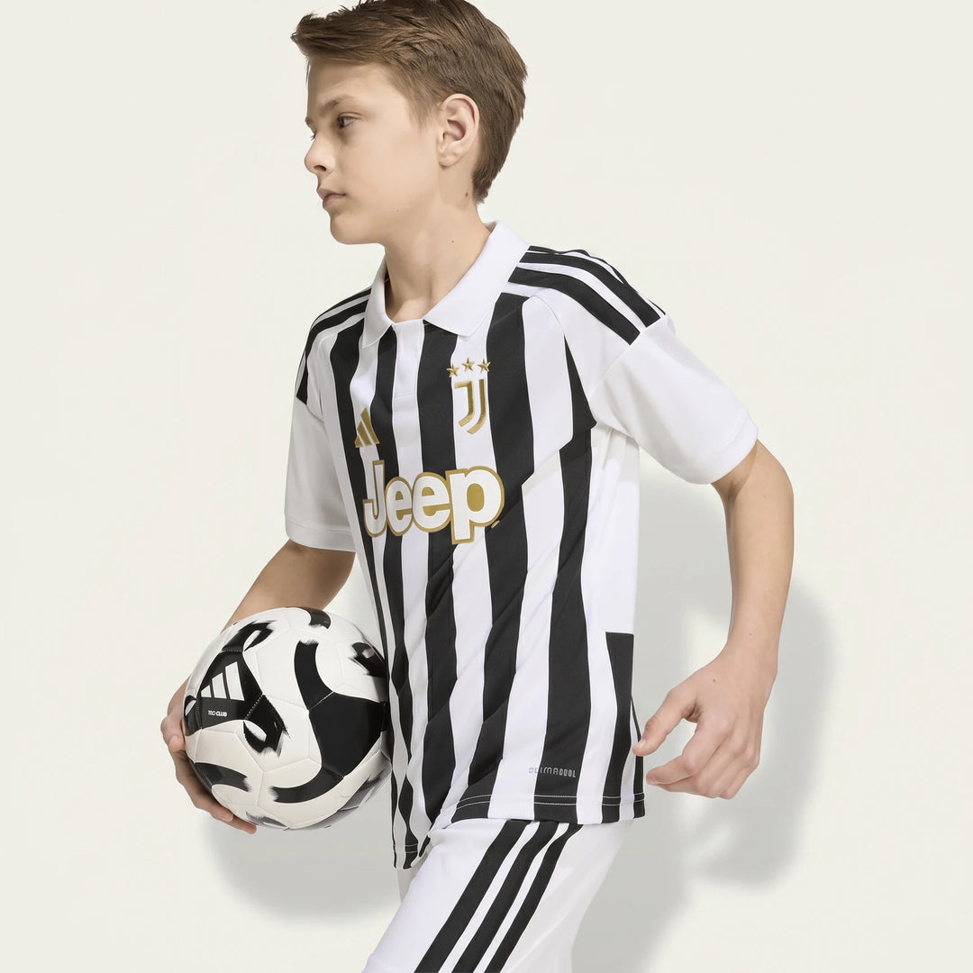 Young boy wearing a black and white striped Adidas Juventus 26/27 Home Jersey, holding a soccer ball.