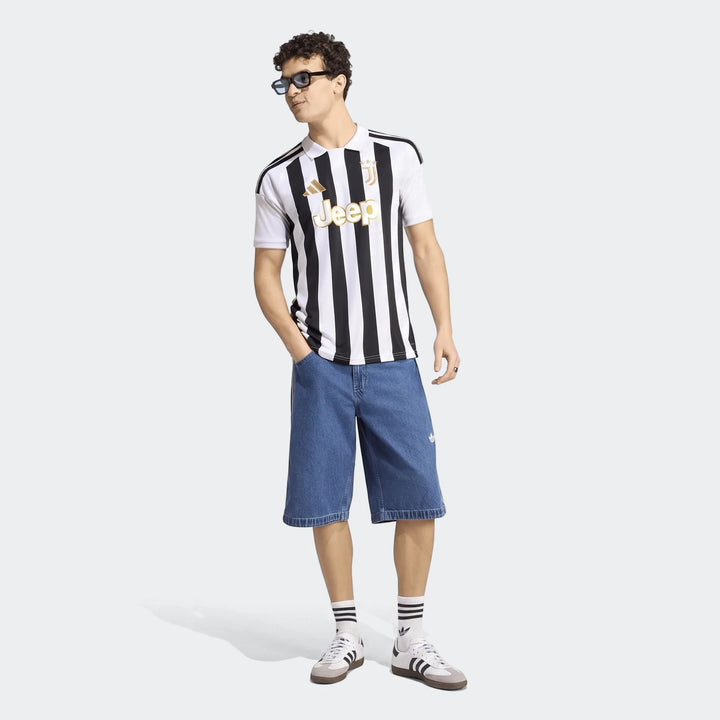 Male model wearing a Juventus 26/27 Home Jersey with black and white stripes, blue denim shorts, white socks, and white