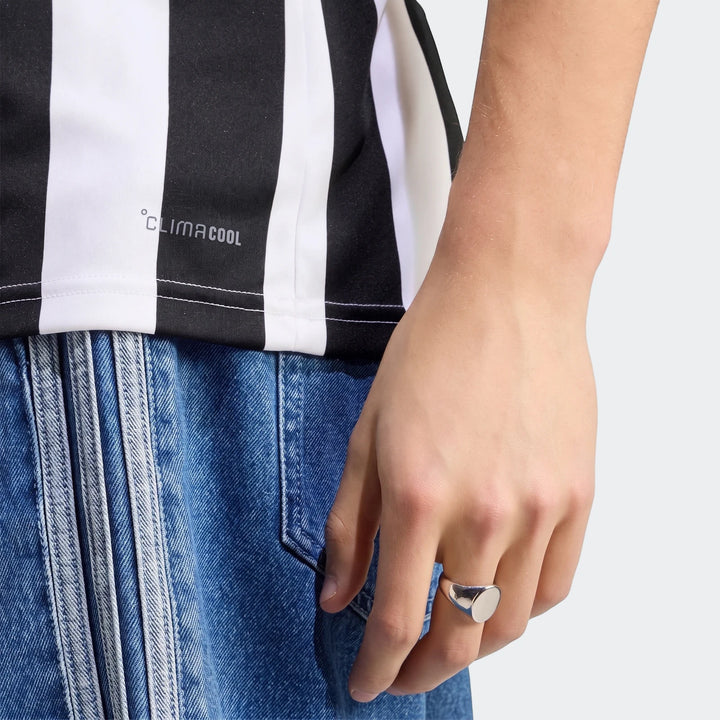 Close-up of a person wearing a black and white striped Juventus 26/27 Home Jersey and blue denim jeans, featuring a silver
