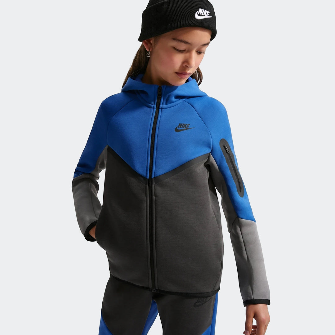 Young girl wearing a blue, grey, and black Nike Air Tech Fleece hoodie and matching sweatpants. Hands in pockets and beanie.