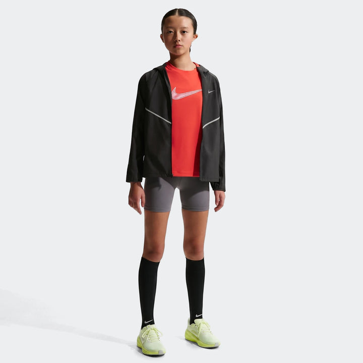 Young girl wears a black Nike+ Repl Miler jacket over a red t-shirt, gray shorts, and neon yellow shoes, full body.