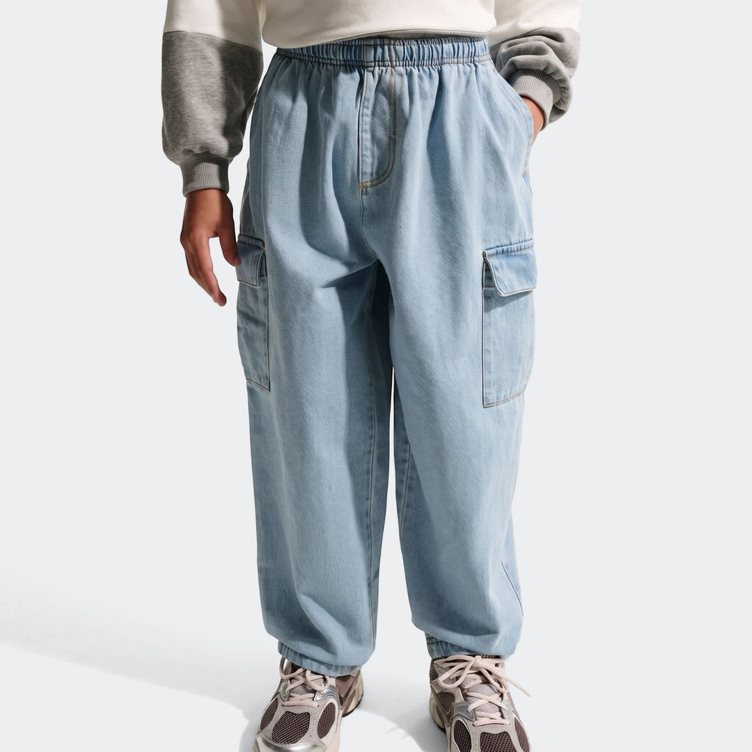 A person wearing light blue denim cargo pants with an elastic waist, visible cargo pockets, and sneakers, shot from the