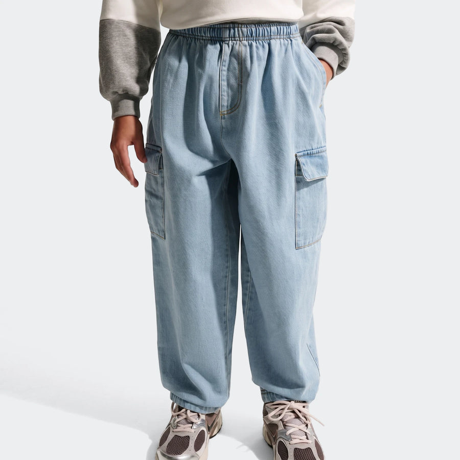 A person wearing light blue denim cargo pants with an elastic waist, visible cargo pockets, and sneakers, shot from the