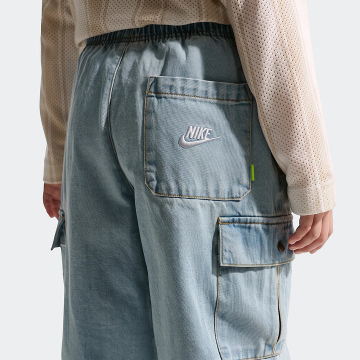 Close-up back view of Nike K NSW light blue denim cargo pants, featuring an elastic waistband and embroidered Nike logo.