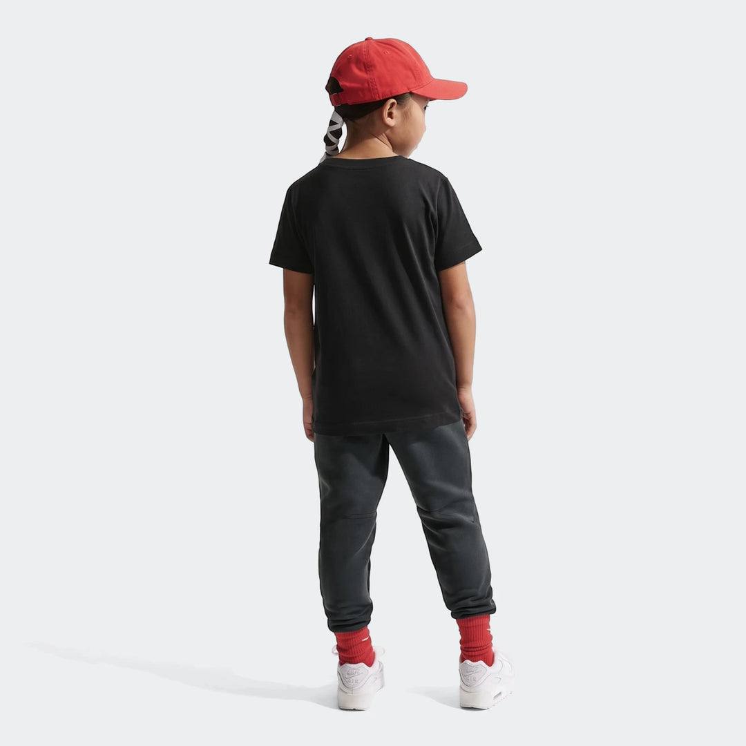 Child wearing a K Nsw Tee Boxy Black T-shirt, dark gray sweatpants, red cap, and white sneakers, photographed from behind.