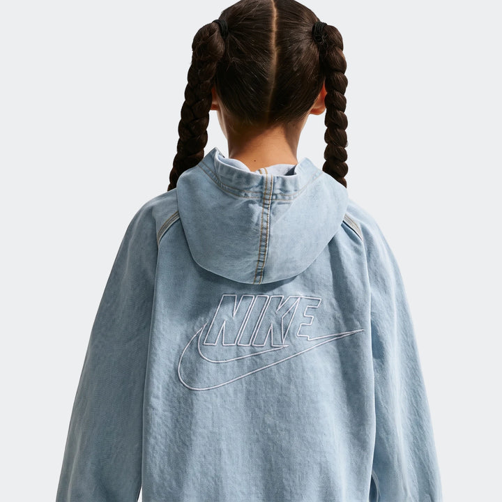 Back view of a child wearing a light blue Nike denim hooded full-zip jacket with a white embroidered logo and braided hair.