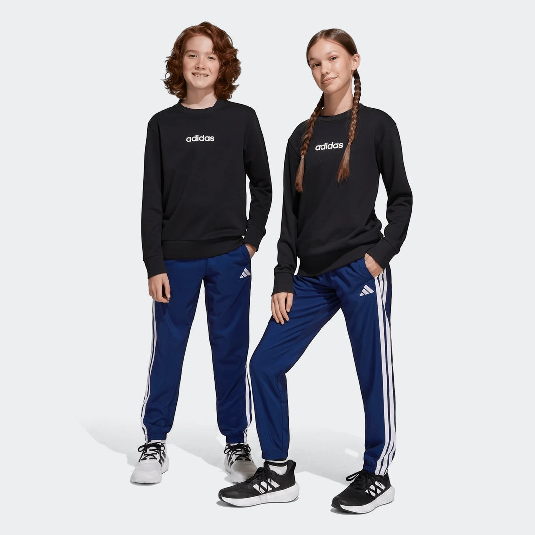 Two kids in black Adidas long-sleeve sweatshirts and blue Adidas Essentials Climacool Tracksuit Bottoms, featuring white