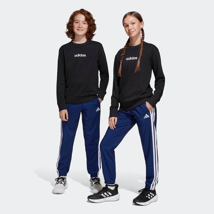 Two kids in black Adidas long-sleeve sweatshirts and blue Adidas Essentials Climacool Tracksuit Bottoms, featuring white