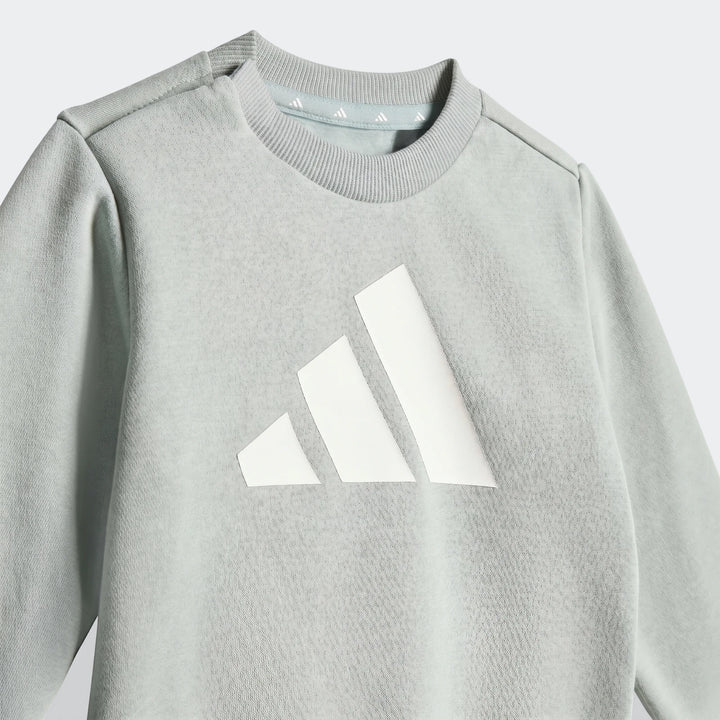 Kids Adidas Essentials light green long-sleeve sweatshirt, featuring a prominent white three-bar logo, shown in a close-up