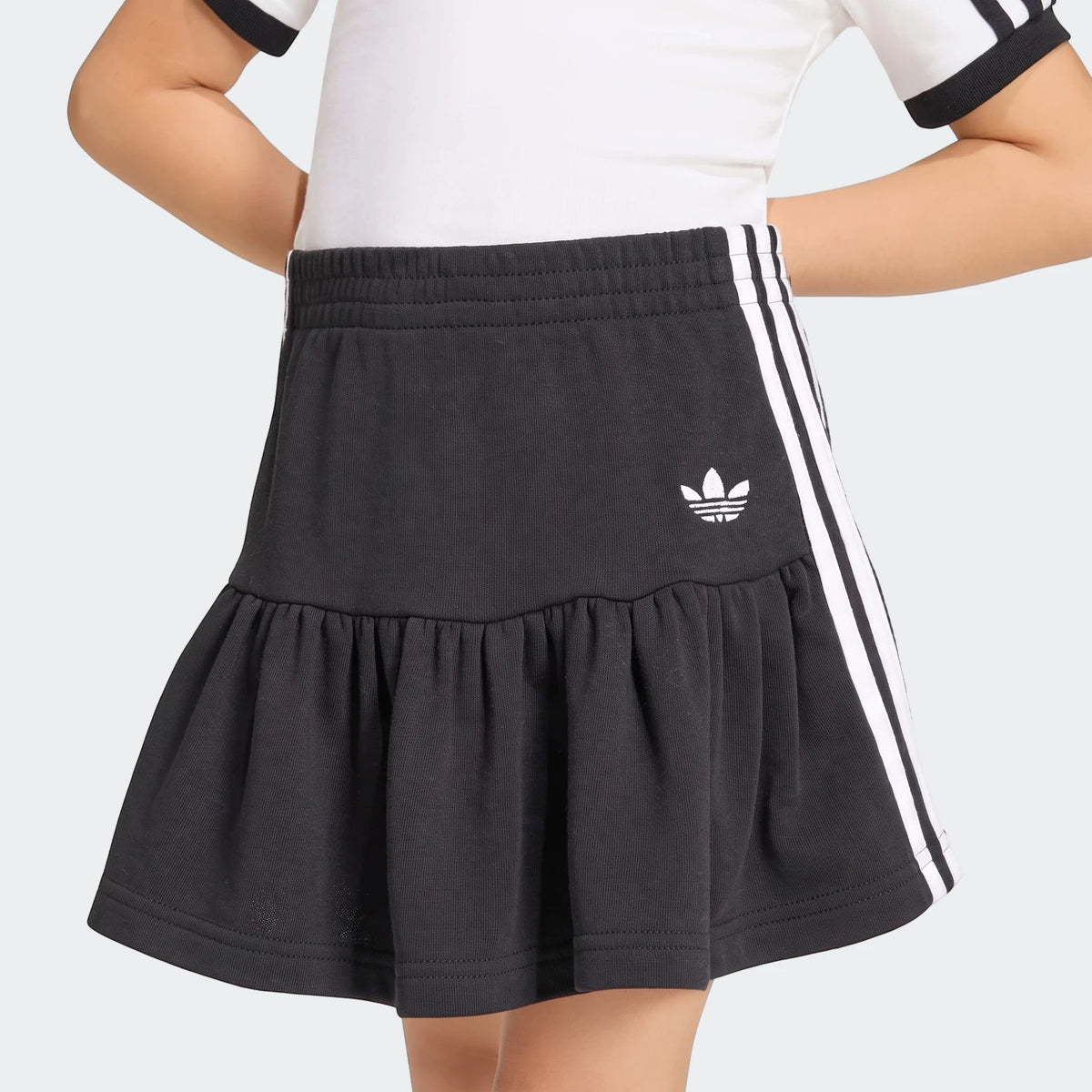 Kids black Adidas 3-Stripes skirt and white t-shirt set, shown worn by a child from waist-up.