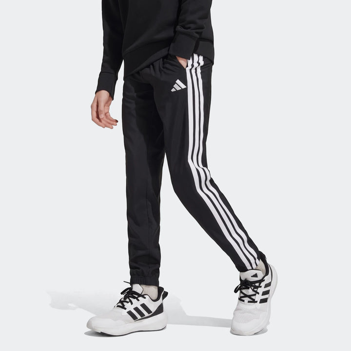 Kids black Adidas Essentials Climacool tracksuit bottoms with white 3-stripes, shown worn with white sneakers in a walking