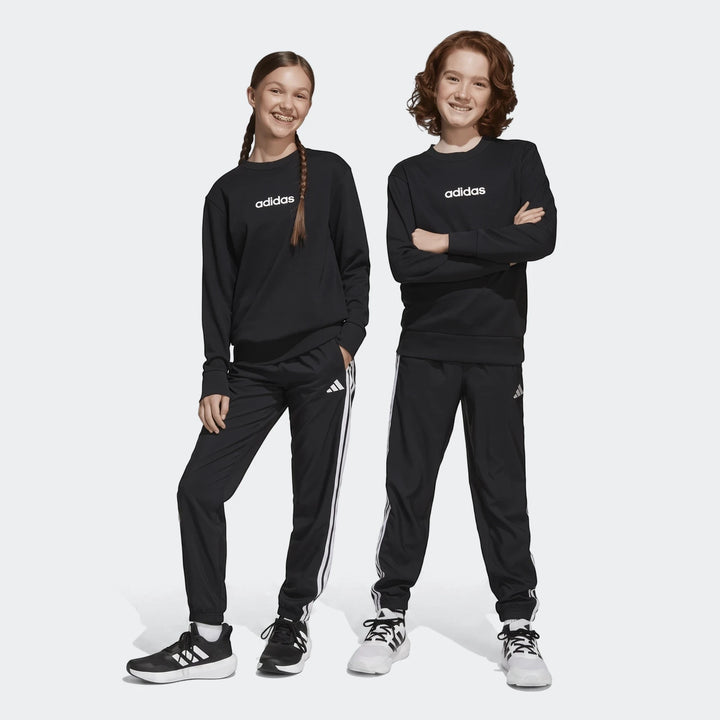 Two children in black Adidas Essentials Climacool tracksuits with white stripes and logos, smiling on a white background.