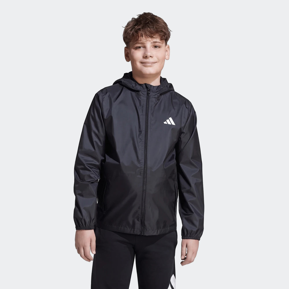 Kids black Adidas rain jacket, modeled by a boy, featuring a hood, full zip closure, and the iconic three-bar logo.
