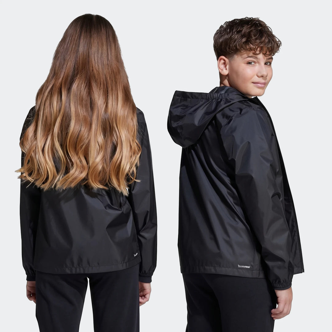 Two kids wearing black rain jackets, with a girl showing the back view and a boy showing a side view.