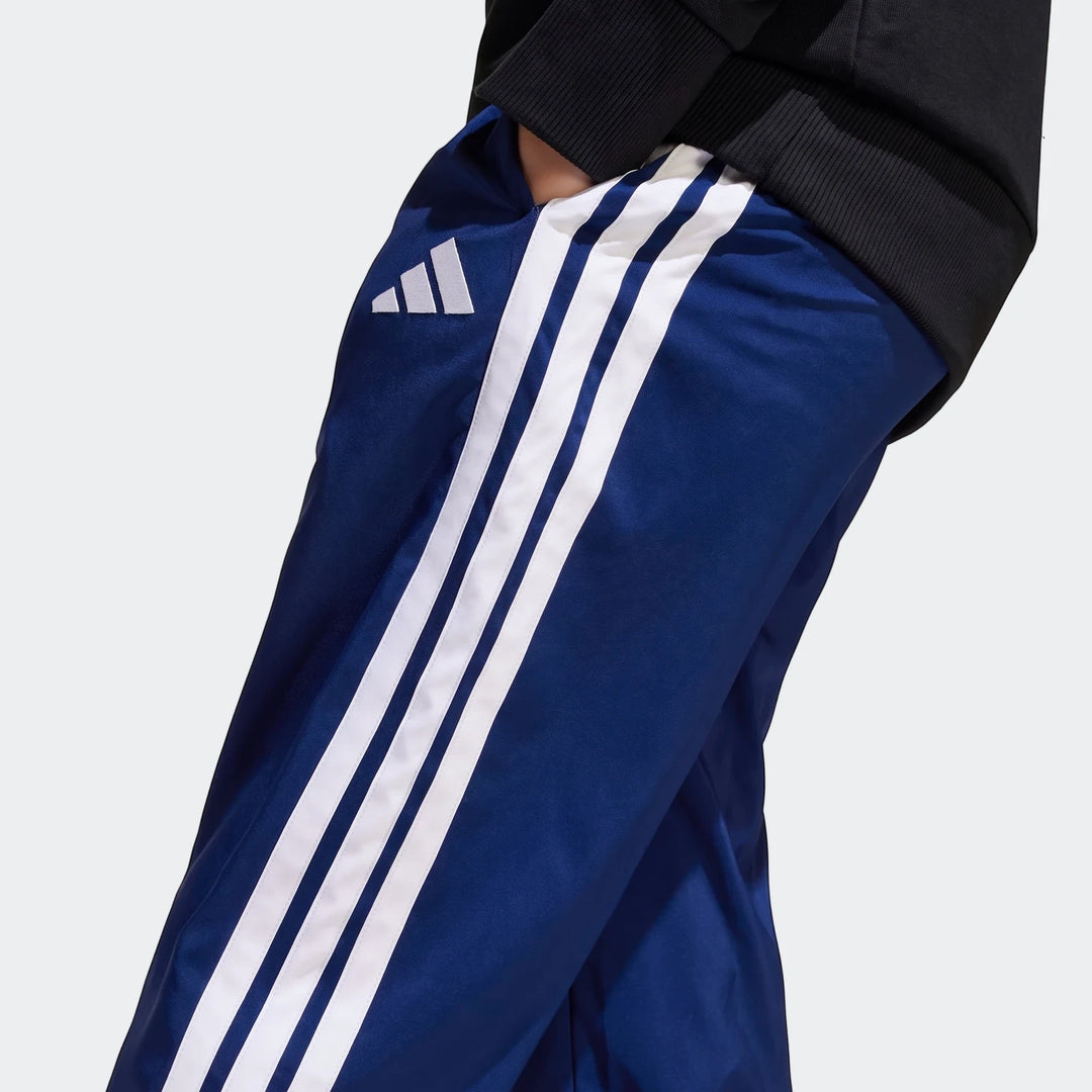 Kids blue Adidas Essentials Climacool tracksuit bottoms with white three stripes and logo, worn by a person with a hand in