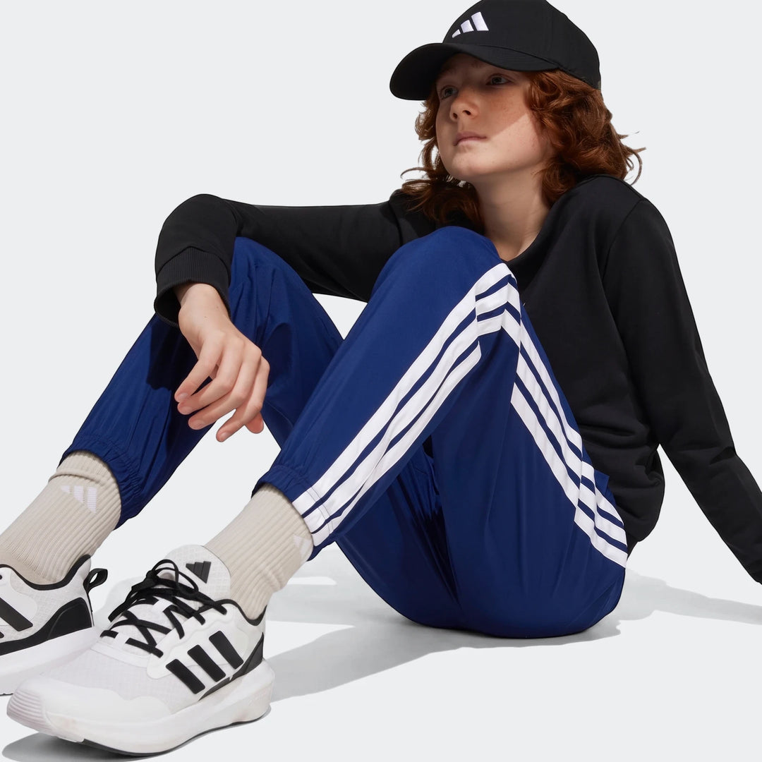Kids' Essentials Climacool Tracksuit Bottoms in blue with white stripes, worn by a child with a black cap and white