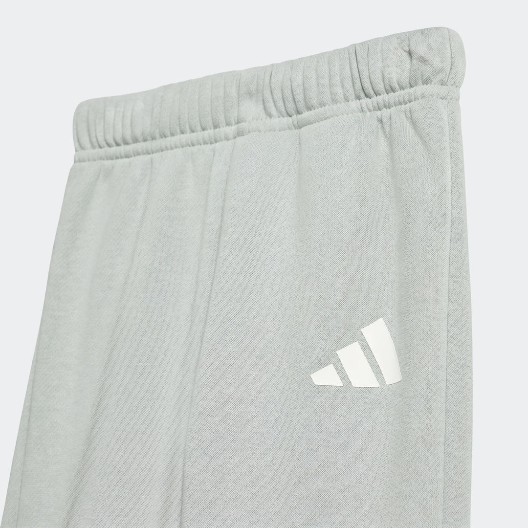 Close-up of Kids Essentials Joggers in light grey with a white Adidas logo, showing the elastic waistband and fabric.